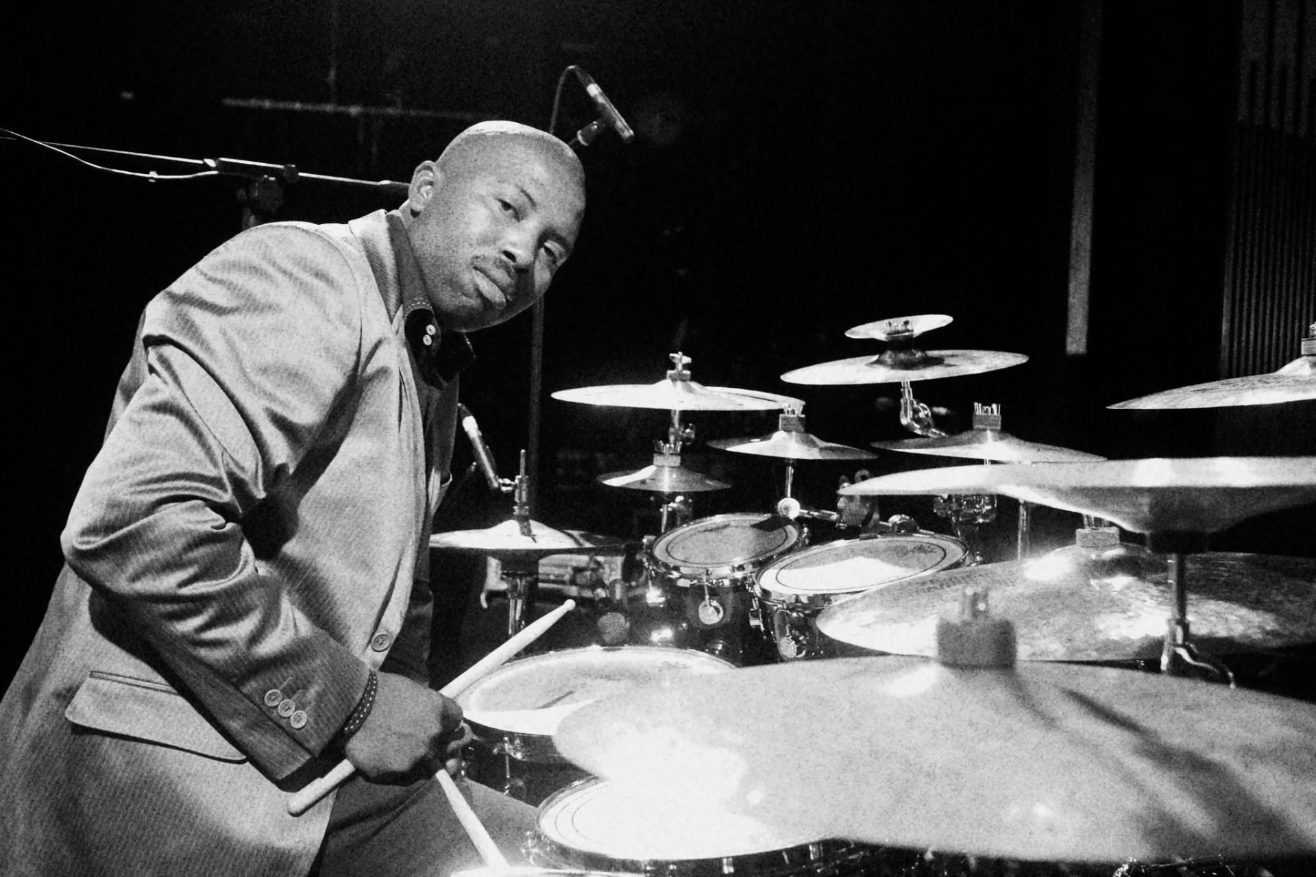 Black-and-white portrait of Sipho behind the kit, sticks in hand